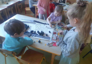 Dzieci przy użyciu różnych materiałów wykonują wspólną prace plastyczną