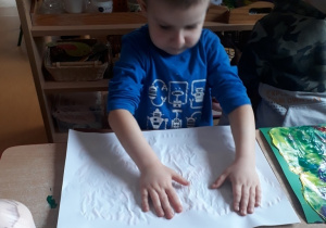 chłopiec rozciera rękami farbę znajdującą się pod kartką