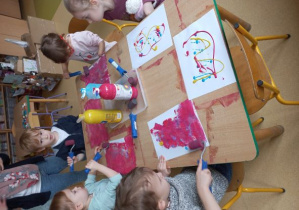 Dzieci na kartce papieru mieszają kolory farb wałkiem