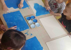 Dzieci przygotowują niebieskie tło do pracy plastycznej