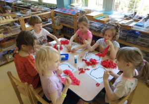 Dzieci siedzą przy stoliku i formują kuleczki z bibuły