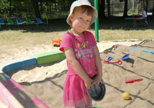 Dziewczynka stoi w piaskownicy i pozuje do zdjęcia