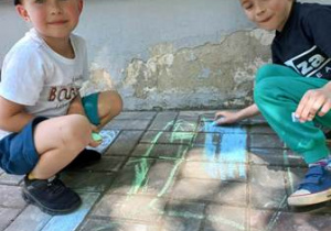 Kajetan i Franio malują kredami taras przedszkolny