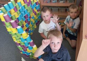 Chłopcy w czasie zabaw swobodnych na dywanie konstruują domek z papierowych kubeczków