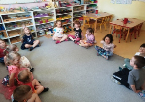 Dzieci siedzą na dywanie w kręgu z zamkniętymi oczami