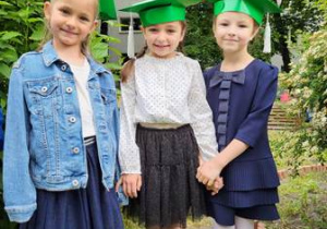Trzy dziewczynki w zielonych biretach stoją obok siebie i pozują do pamiątkowego zdjęcia