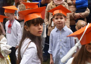 chłopiec i dziewczynka pozują do zdjęcia w pomarańczowych biretach