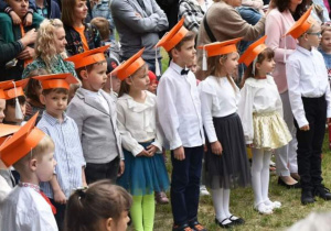 grupa dzieci żegnających przedszkole w pomarańczowych biretach