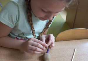 Dziewczynka dokłada do ślimaka uformowanego z plasteliny wykałaczki tworząc czułki