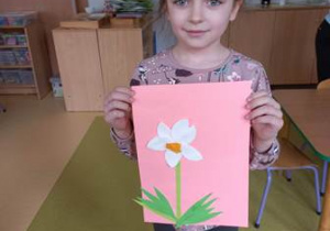 Nela prezentuje gotową pracę plastyczną - kwiatek zrobiony przy użyciu wacików kosmetycznych oraz fragmentów bibuły i zielonego papieru kolorowego