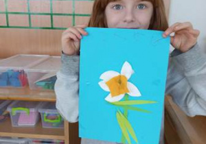 Chłopiec trzyma w dłoniach ukończoną przez siebie prace plastyczną przedstawiającą wiosenny kwiat
