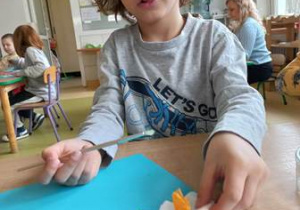Chłopiec w czasie wykonywania pracy plastycznej dokleja elementy kwiatka na kartkę papieru