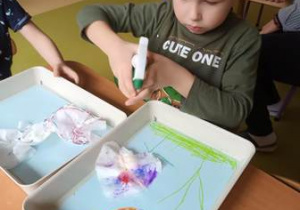Chłopiec spryskuje wodą swoją prace plastyczną i uwalnia kolory rozpuszczając barwniki z nakreślonych mazakami linii