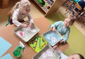 Dzieci siedzą przy stoliku i barwią chusteczki higieniczne mazakami