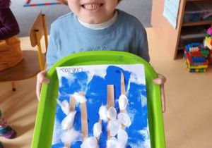 Chłopiec prezentuje wykonaną przez siebie pracę plastyczną zatytułowaną "Wielkanocne kotki"