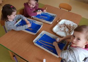 Dziewczynki w czasie wykonywania pracy plastycznej naklejają bazie z elementów kolorowego papieru na granatowe tło