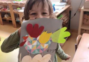 Chłopiec prezentuje wykonaną przez siebie pracę plastyczną przedstawiająca kolorową kurkę