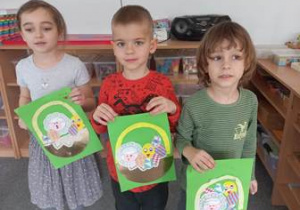 Troje dzieci przedstawia wykonane przez siebie prace plastyczne pt. "Wielkanocny koszyczek"