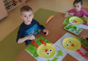 Chłopiec i dziewczynka wykonują przy stoliku pracę plastyczną "Wielkanocny kurczaczek"