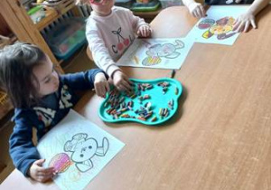 Dzieci młodsze kolorują pastelami malowankę przedstawiającą wielkanocnego zajączka