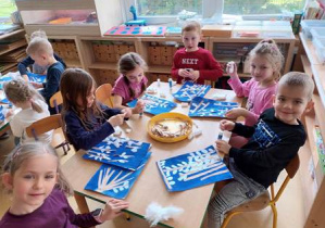 Dzieci przy stoliku pozują do zdjęcia w czasie wykonywania pracy plastycznej "Wielkanocne kotki"