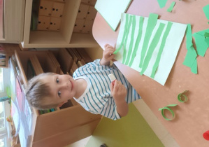 Natan nakleja na kartkę papieru wydarte paski zielonego papieru imitujące trawę
