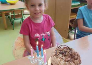 Antosia siedzi przy stole i pozuje do pamiątkowego zdjęcia z urodzinowym tortem