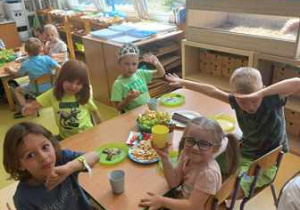 Dzieci siedzą przy stoliczkach i jedzą urodzinowy poczęstunek