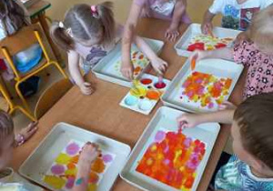 Grupa dzieci przy stoliku zakrapla różnymi kolorami farb chusteczki higieniczne