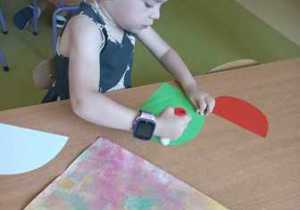 Dziewczynka w czasie wykonywania jednego z etapów pracy plastycznej smaruje klejem elementy kolorowego papieru
