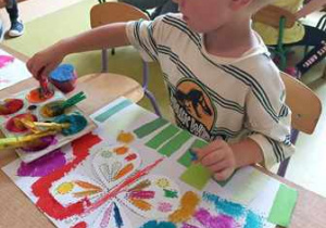 Chłopiec stempluje farbami tło do swojej pracy plastycznej pt. "Motyl"