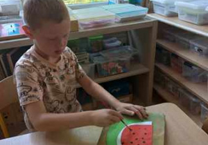Chłopiec maluje czarną farbą pestki arbuza na swojej pracy plastycznej