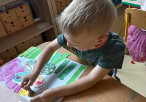 Chłopiec stempluje farbami tło swojej pracy plastycznej