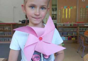 Zuzia pozuje do zdjęcia z wykonanym własnoręcznie wiatraczkiem z kolorowego papieru