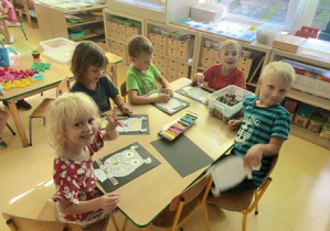 Grupa dzieci siedzi przy stoliku w czasie wykonywania pracy plastycznej z wykorzystaniem plastelinowych kulek