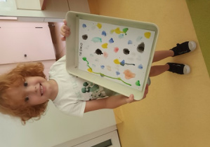 Chłopiec prezentuje namalowane przez siebie tło pracy plastycznej w kolorowe kropki