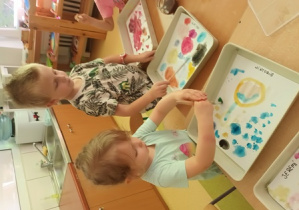 Dzieci przy stoliku malują kolorowe kropki na białym tle