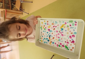 Nina prezentuje namalowane przez siebie farbami kolorowe kropki