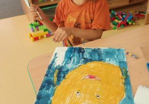 Chłopiec w czasie wykonywania pracy plastycznej pt. "Kropka" - kończy malować tło granatową farbą