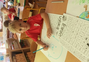 Chłopiec rysuje niebieskim mazakiem "Kropkę" na dużym arkuszu papieru z wykorzystaniem gry matematycznej "Wylosuj mnie"