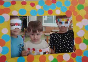 Dzieci pozują do zdjęcia z ramką ozdobioną w kolorowe kropki