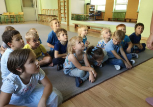 Dzieci siedzą na dywanie i słuchają piosenki