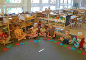 Dzieci siedzą w kręgu i śpiewają piosenkę pokazując kolorowe kropki