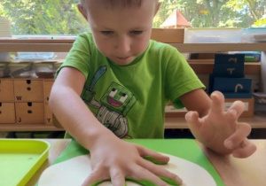 Chłopiec odbija dłoń pomalowaną zieloną farbą na kartonie
