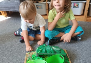 Chłopcy prezentują ułożone przez siebie na podkładce przedmioty w kolorze zielonym odnalezione w sali