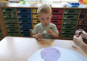 Chłopiec przykleja klejem kropkę na białą kartkę