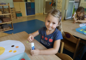 Dziewczynka przykleja kolorowe kropki do białej kartki