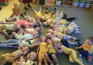Dzieci ubrane na żółto w kolorze grupy odpoczywają na dywanie