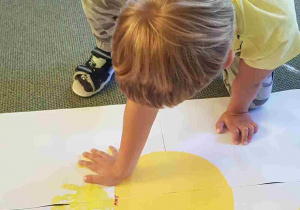 Chłopiec odbija żółtą dłoń na kartonie