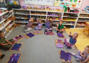 Dzieci siedzą na dywanie i prezentują zebrane przedmioty